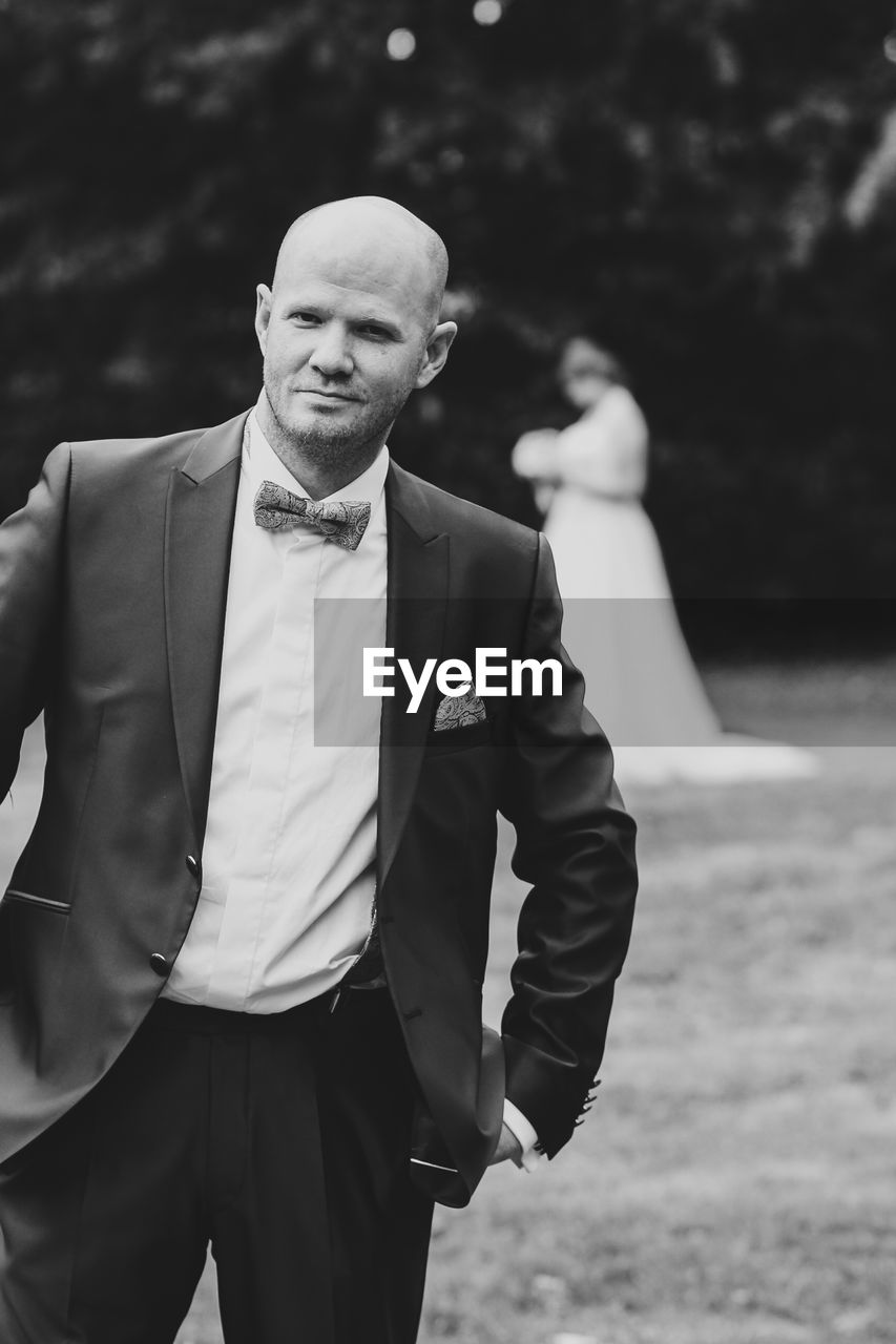 Portrait of completely bald man wearing suit while standing at park