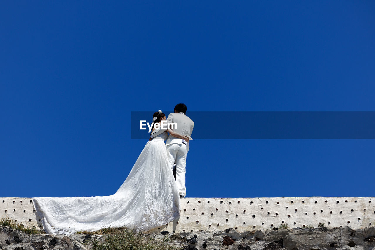 LOW ANGLE VIEW OF MAN AND WOMAN AGAINST BLUE SKY