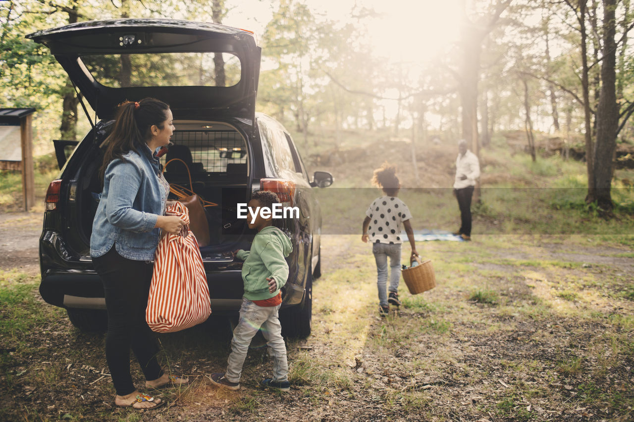 Family unloading luggage from electric car trunk at park