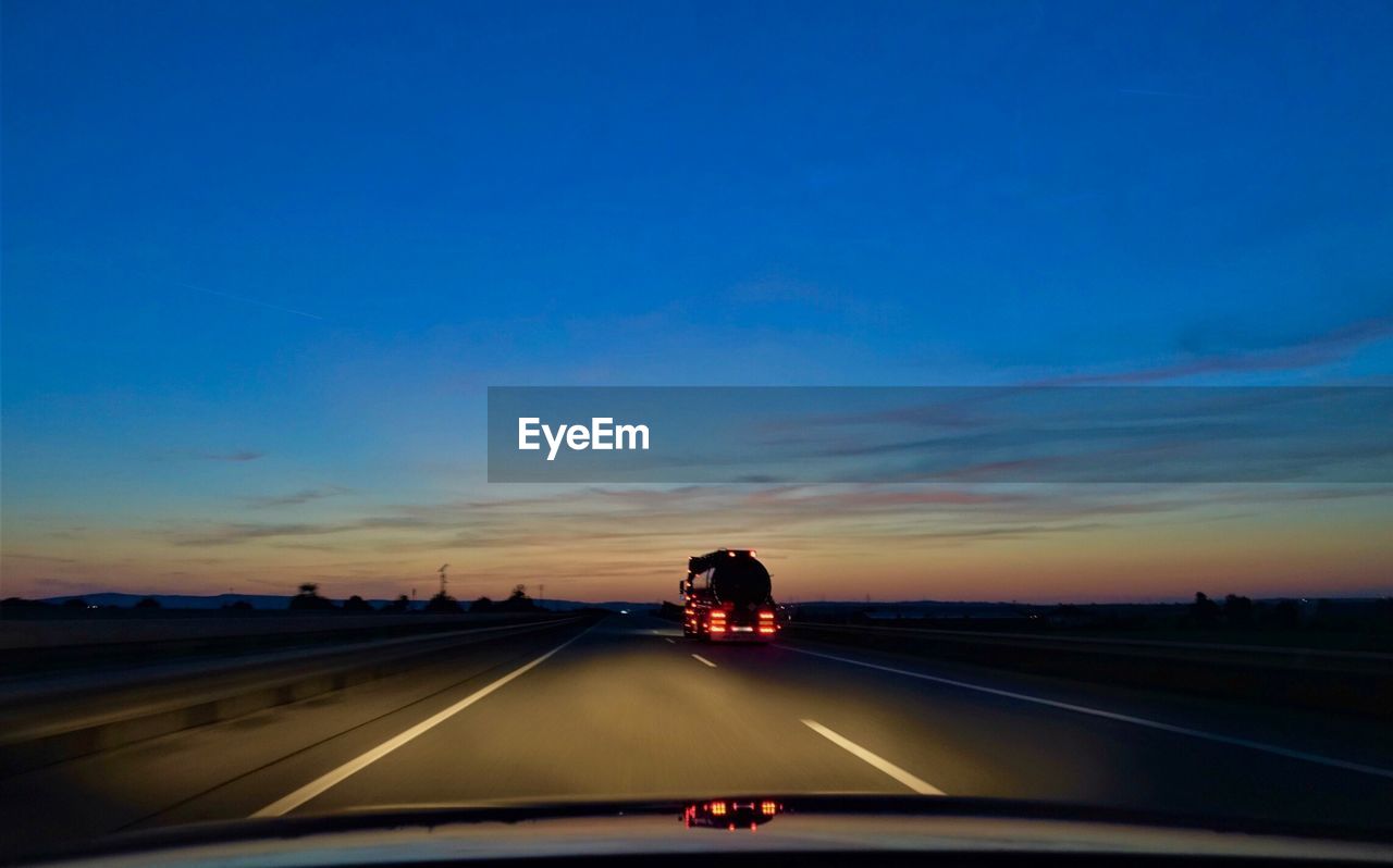 Vehicle on highway against sky during sunset