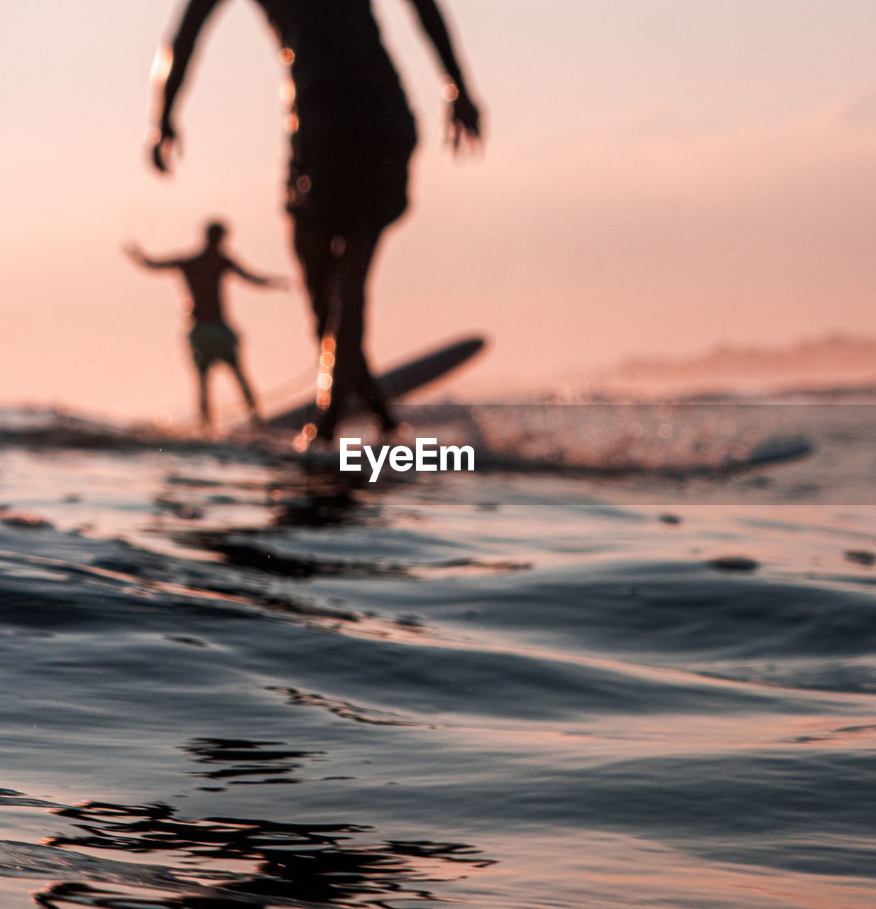 Low section of silhouette people on beach against sky during sunset