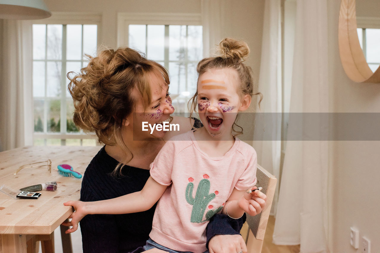Mother and daughter laughing whilst playing with make up at home