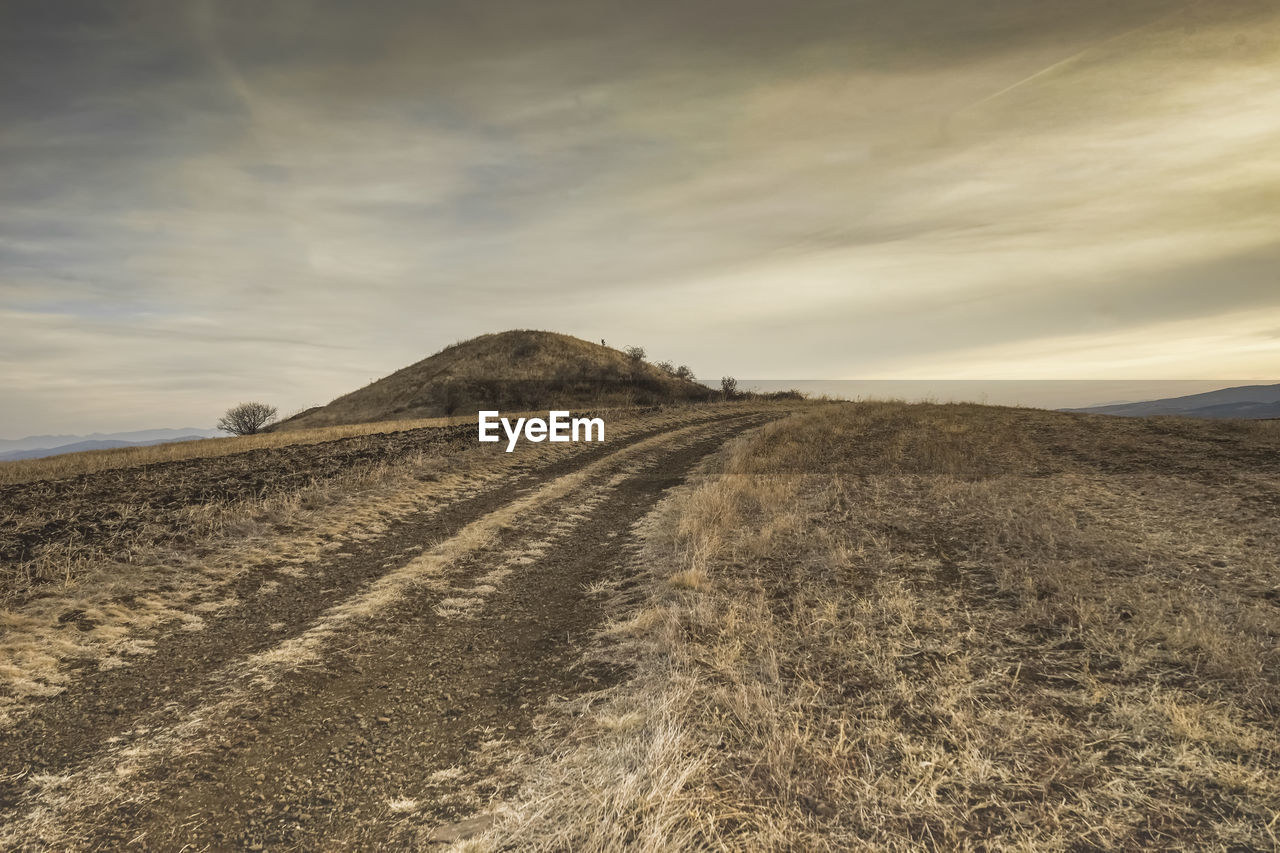 Panoramic view of a burial mound in a filed near a country road with cloudy skies in the background