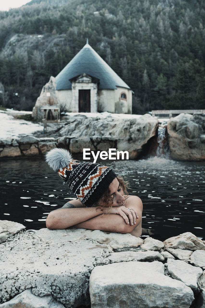 side view of woman sitting on rock by river