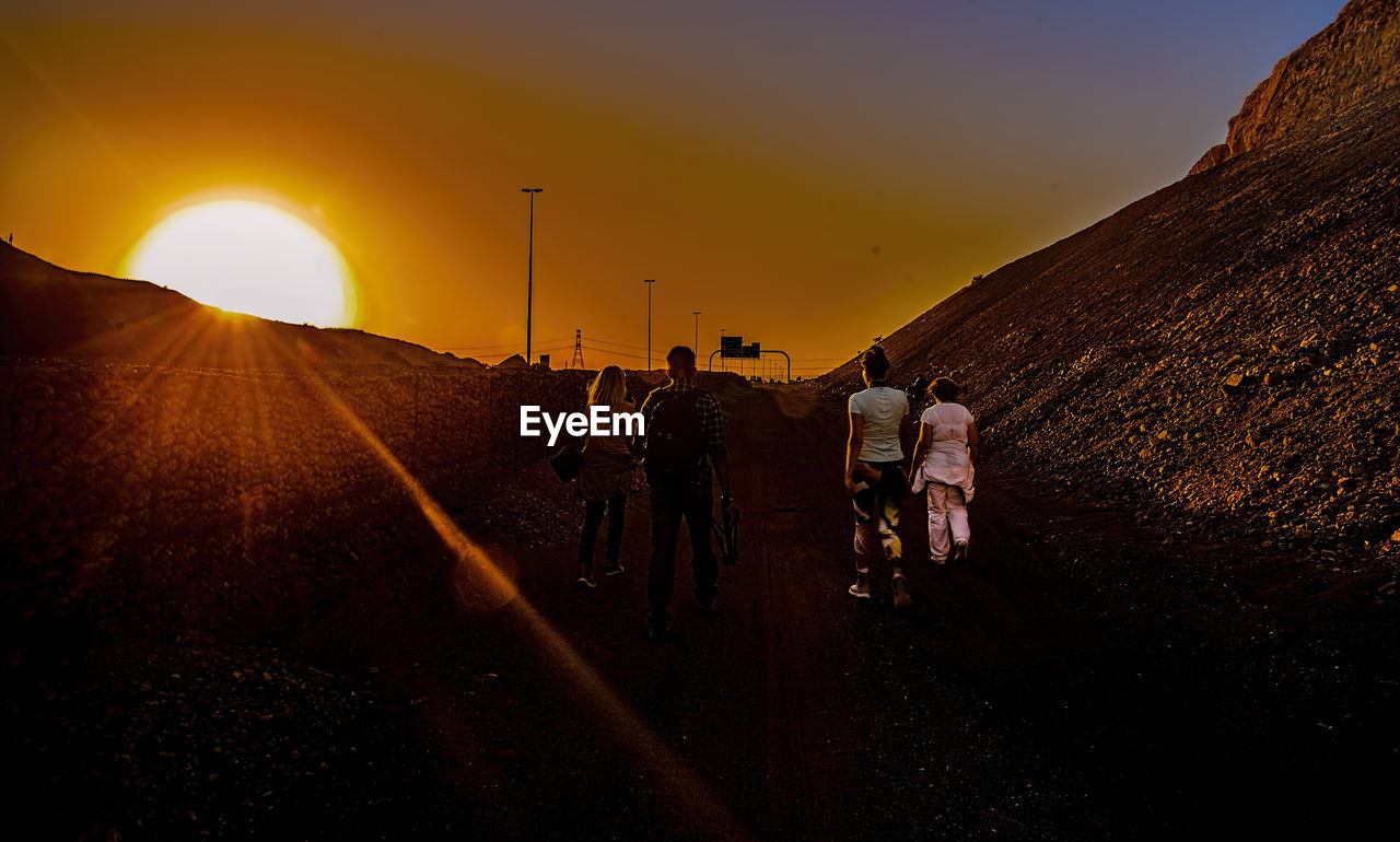 REAR VIEW OF PEOPLE WALKING ON ROAD AGAINST SKY