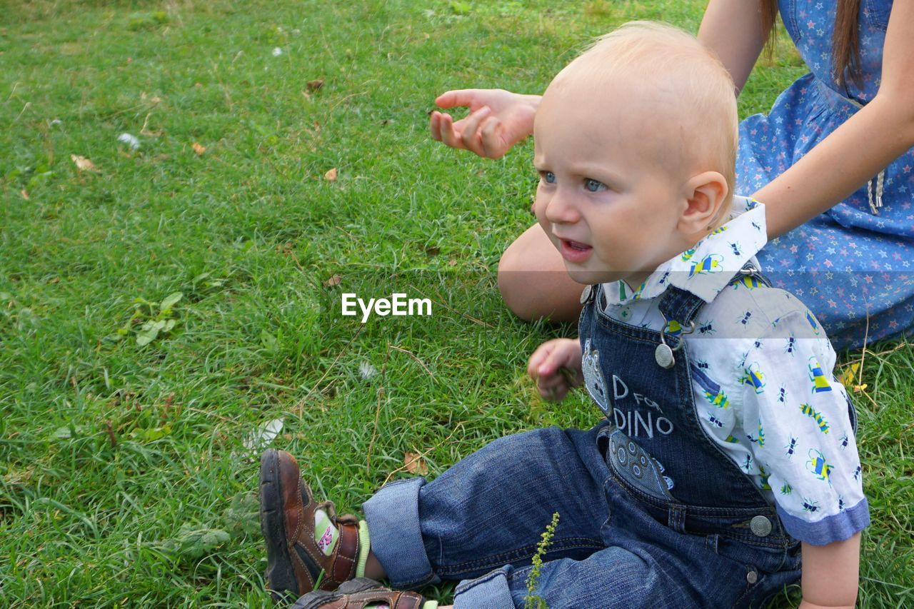 Cute baby boy sitting with mother on grassy field