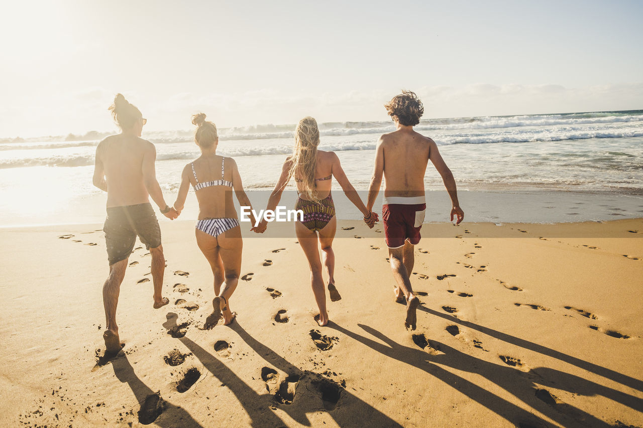 Full length rear view of friends running on beach