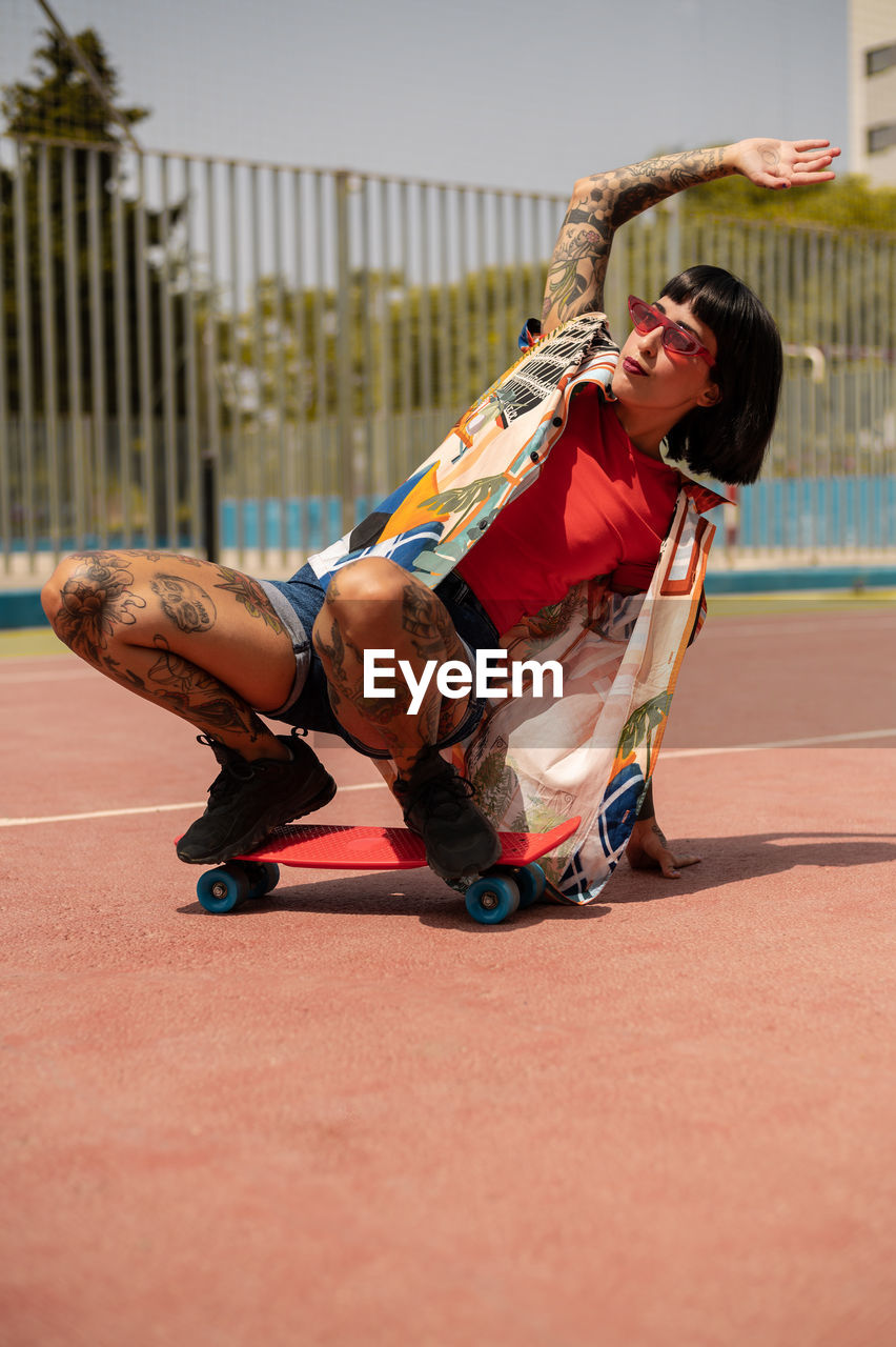 Caucasian girl with tattoos and short black hair on a sports court skating with a skateboard