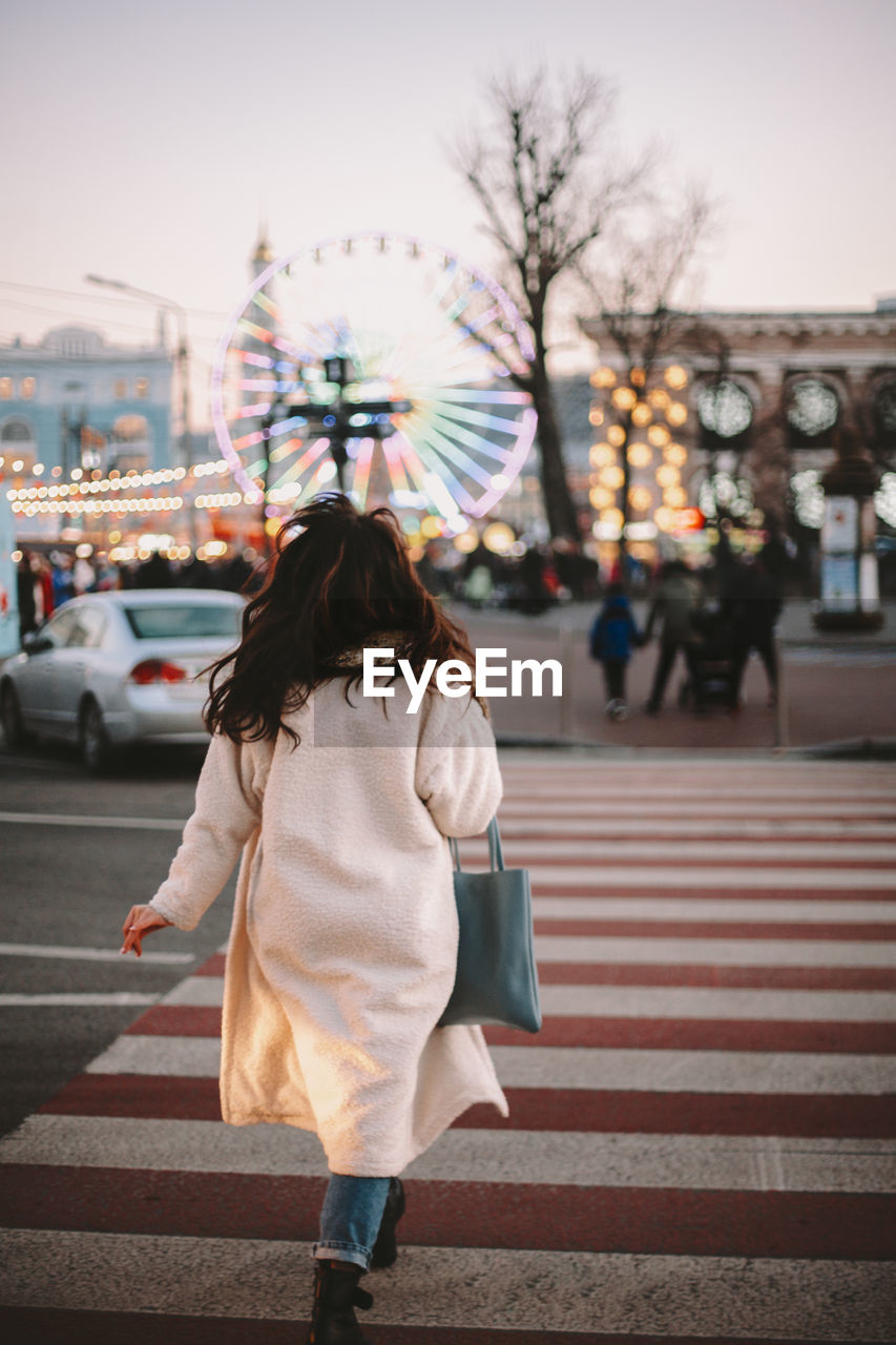 Rear view of young woman crossing road in city in winter