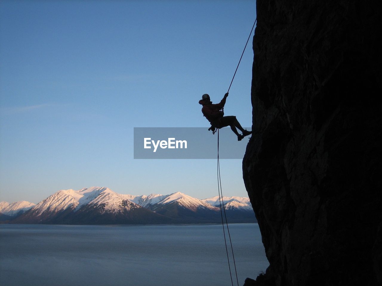 Man rock climbing on cliff against clear blue sky