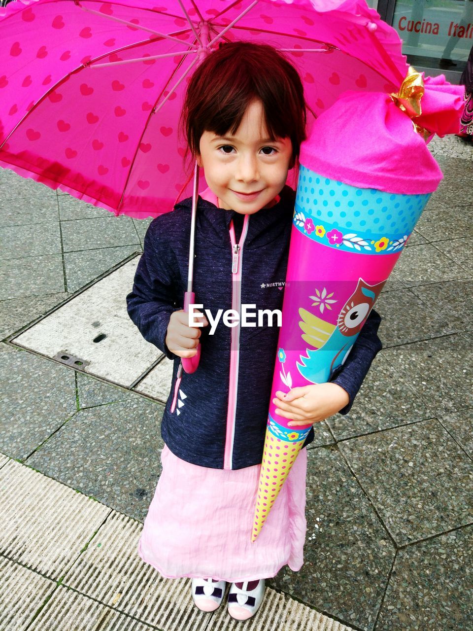 Happy girl holding pink umbrella while standing on road