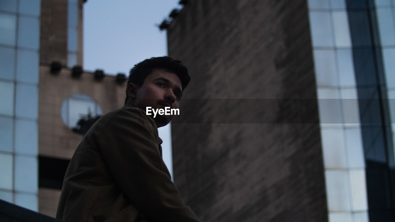 Low angle view of thoughtful young man standing against building in city