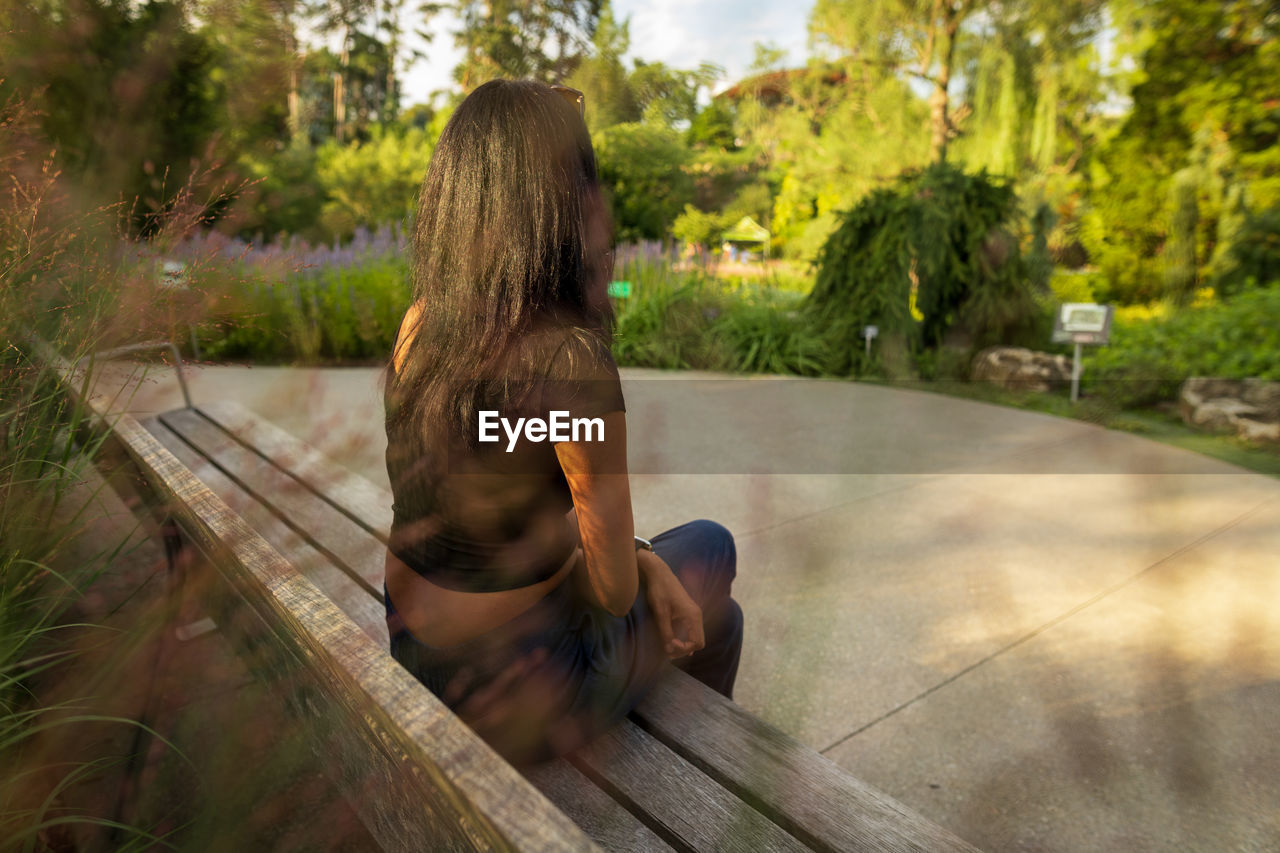 Rear view of woman sitting on park bench in public park