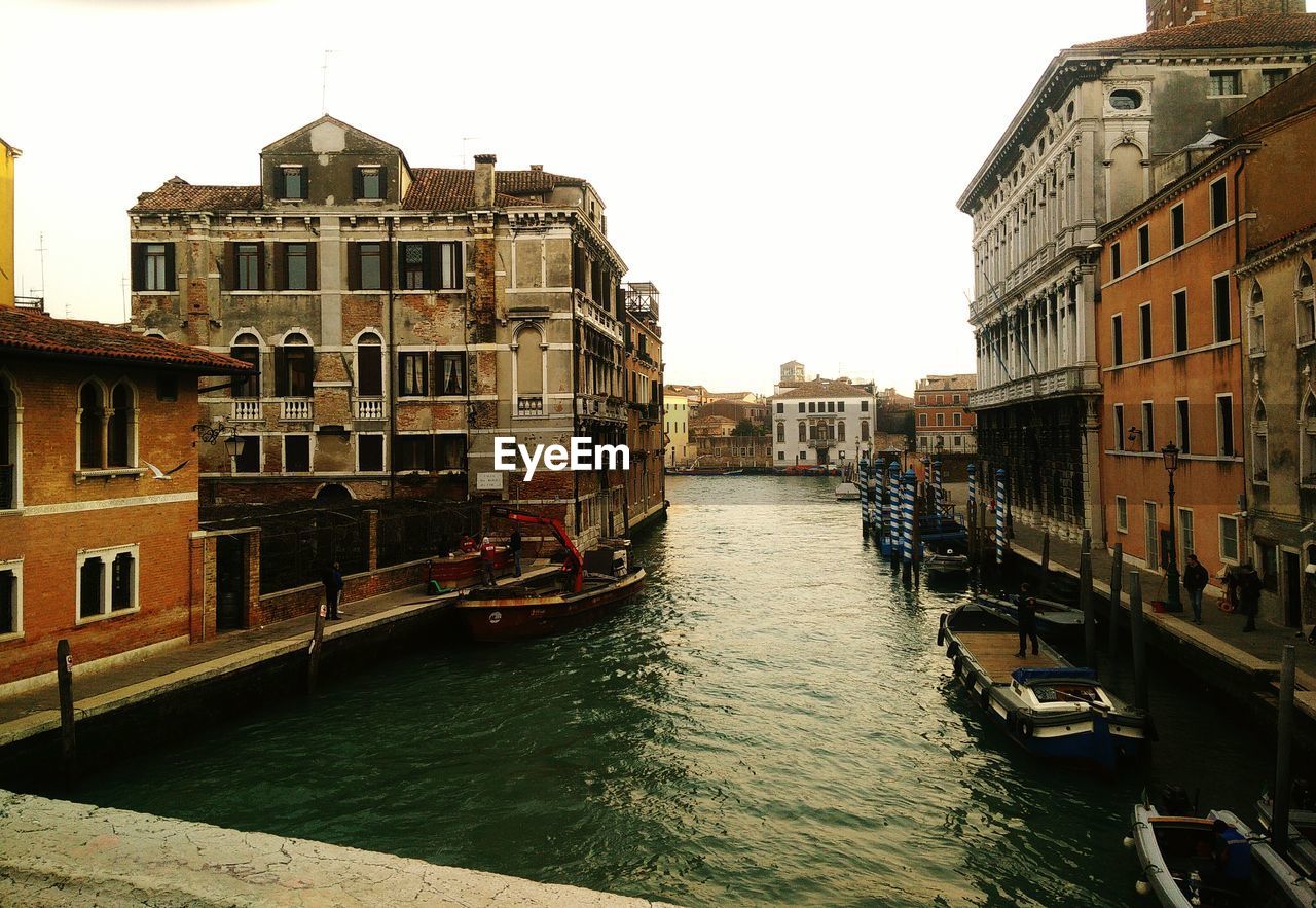Boats moored in canal amidst buildings against sky