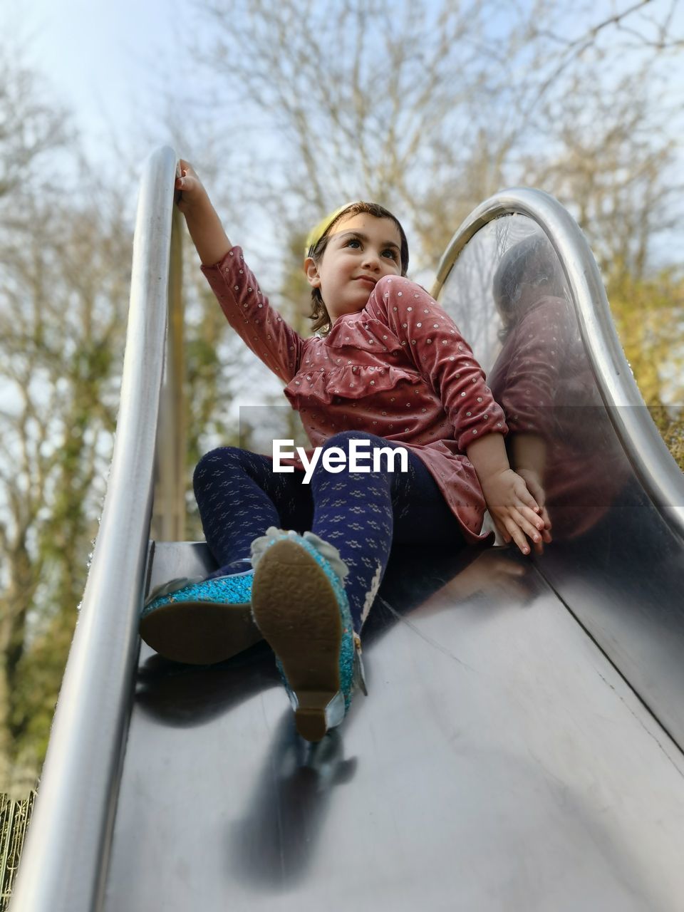 Low angle view of girl sitting on slide at park