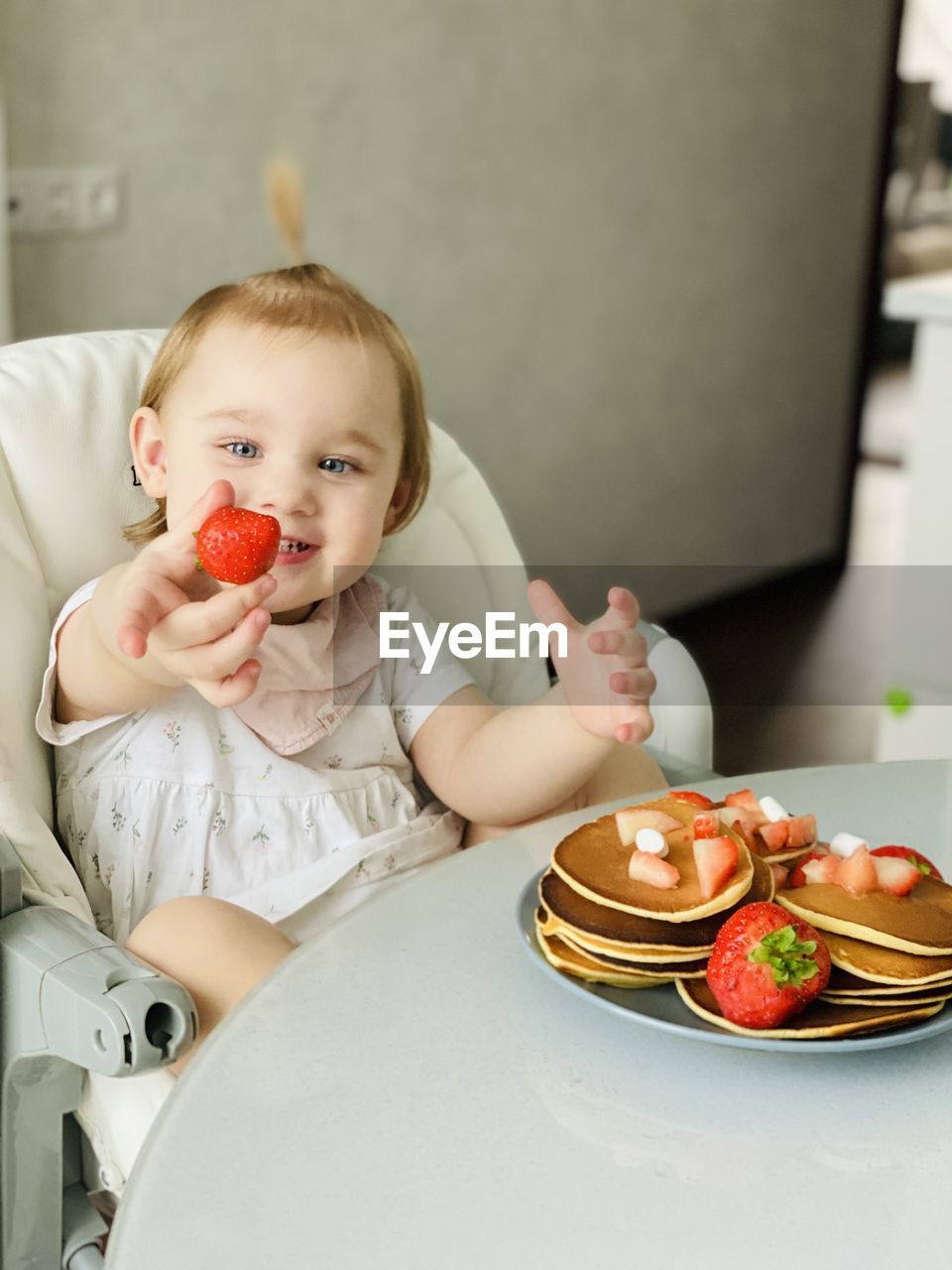 Girl eating berries and pancakes in plate on table
