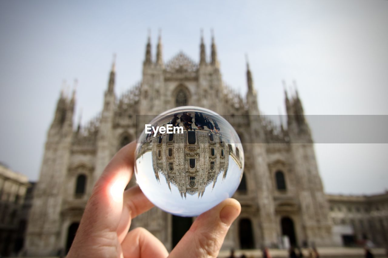 Cropped hand holding crystal ball against milan cathedral 