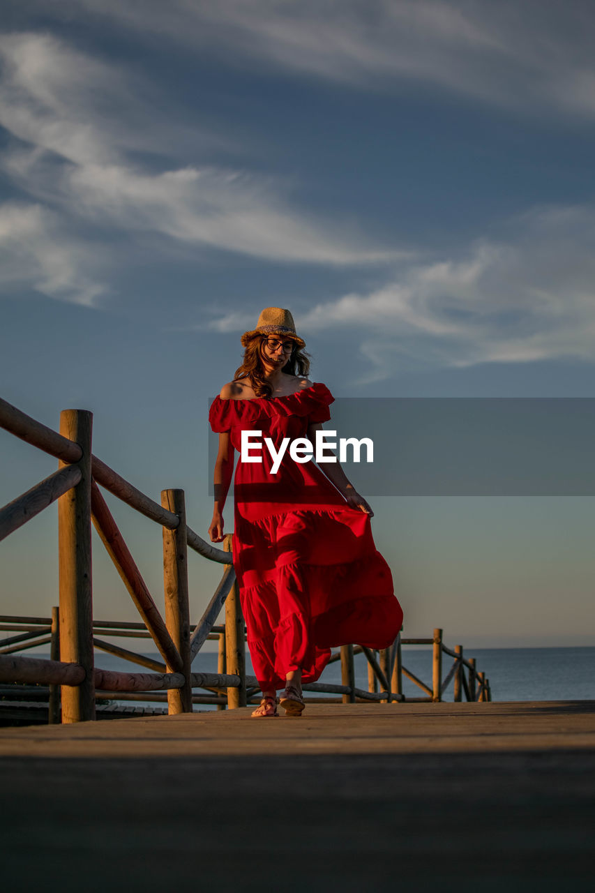 Woman standing on railing by sea against sky