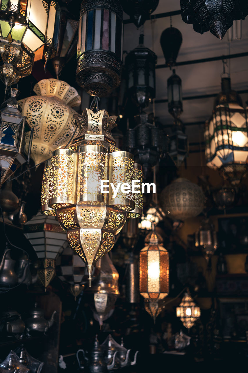 LOW ANGLE VIEW OF ILLUMINATED LANTERNS HANGING ON CEILING AT NIGHT