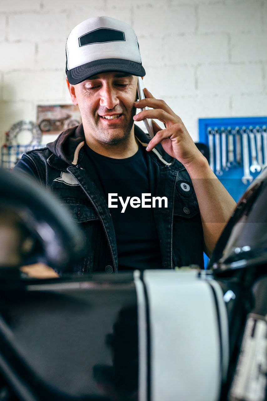 Mechanic talking on phone while standing by car in garage