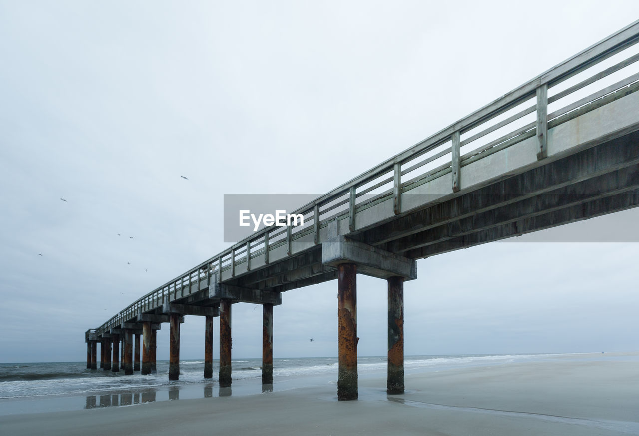 Low angle view of pier at beach against sky