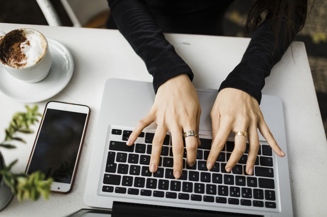 High angle angle view of coffee cup on table and laptop with female hands writting on keyboard