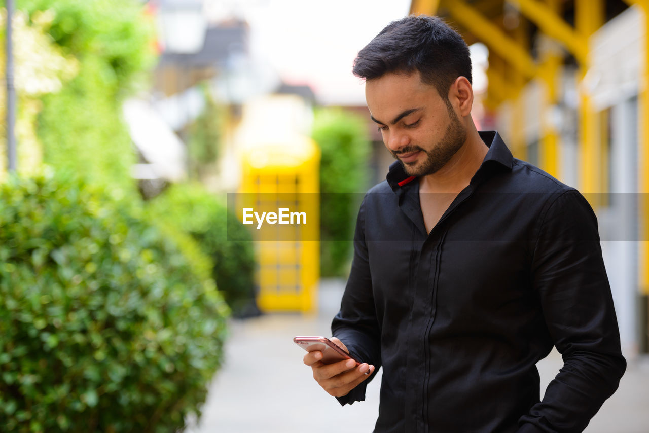 YOUNG MAN USING MOBILE PHONE WHILE STANDING ON CAMERA AT SMART