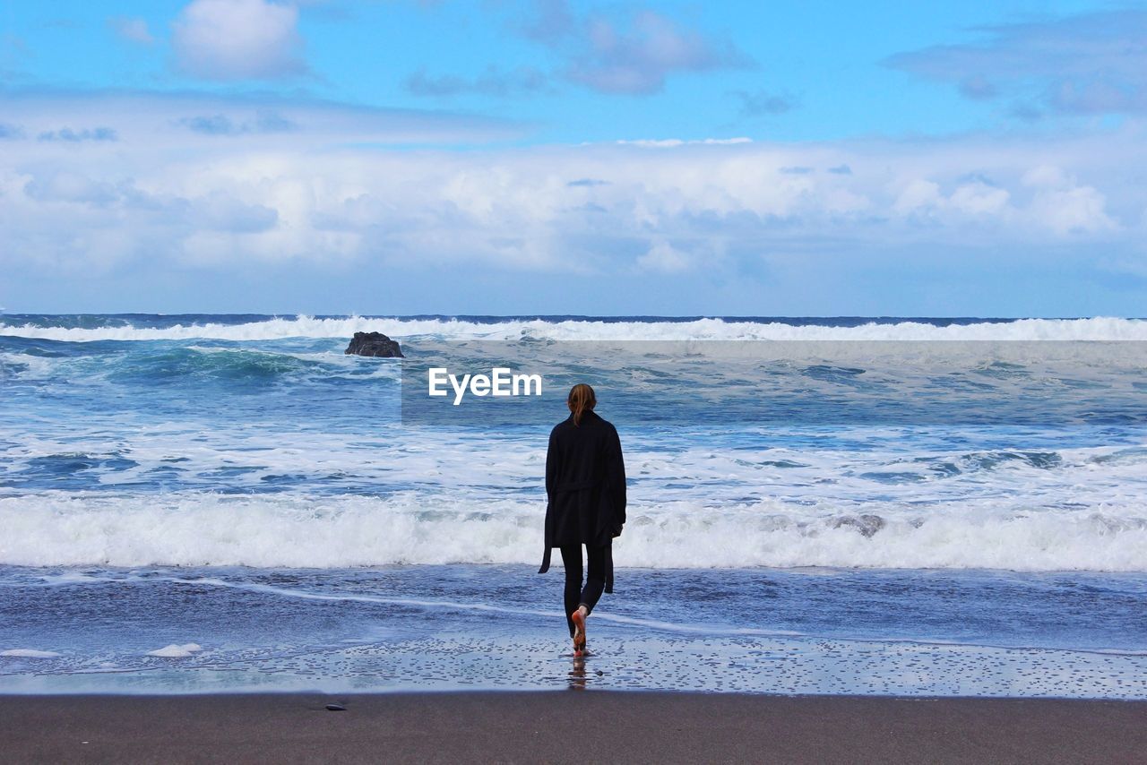 Rear view of woman walking towards sea at beach