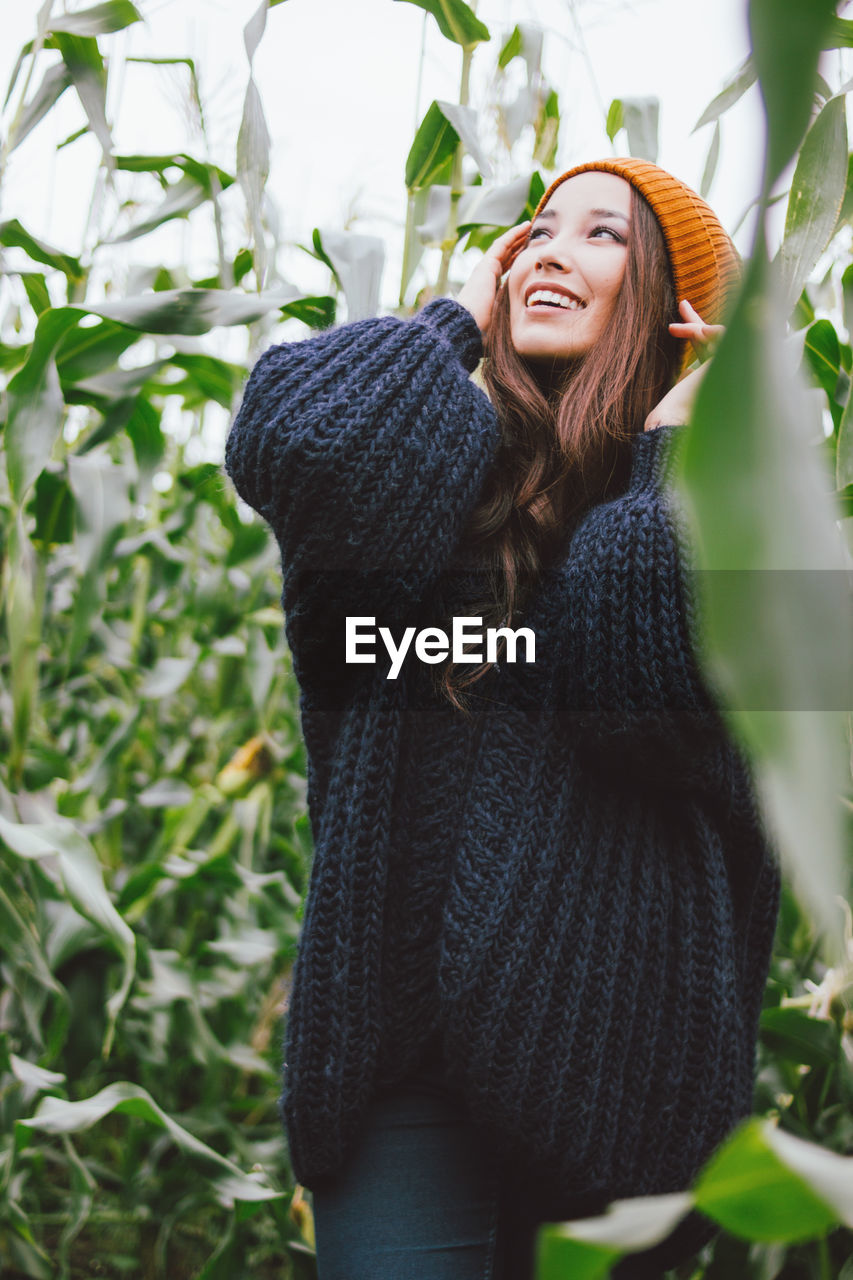 Smiling young woman standing amidst corns on farm