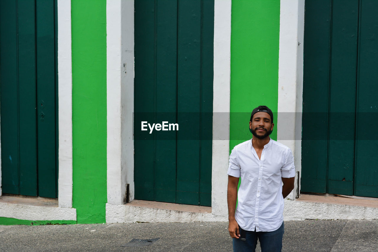 Young man standing against green built structure