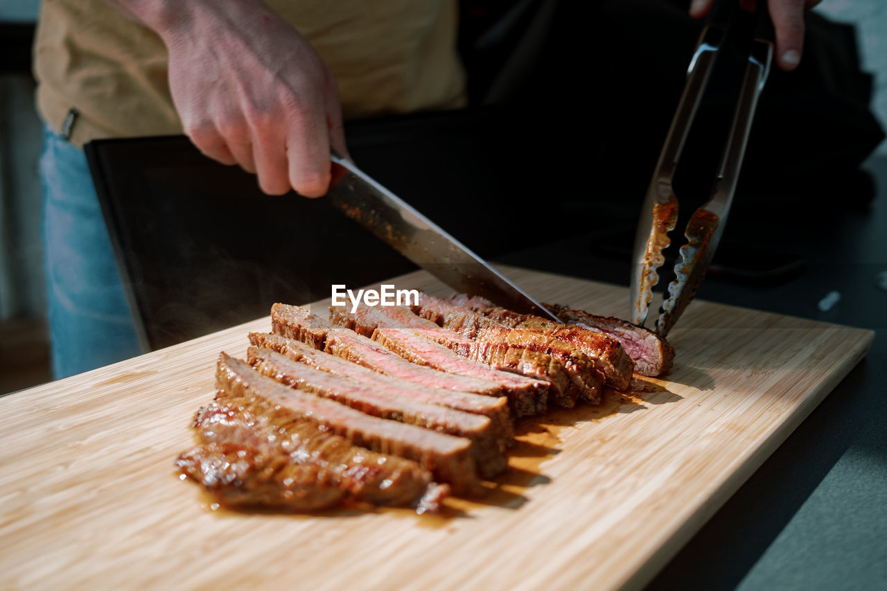 Cropped hand of person slicing meat on table