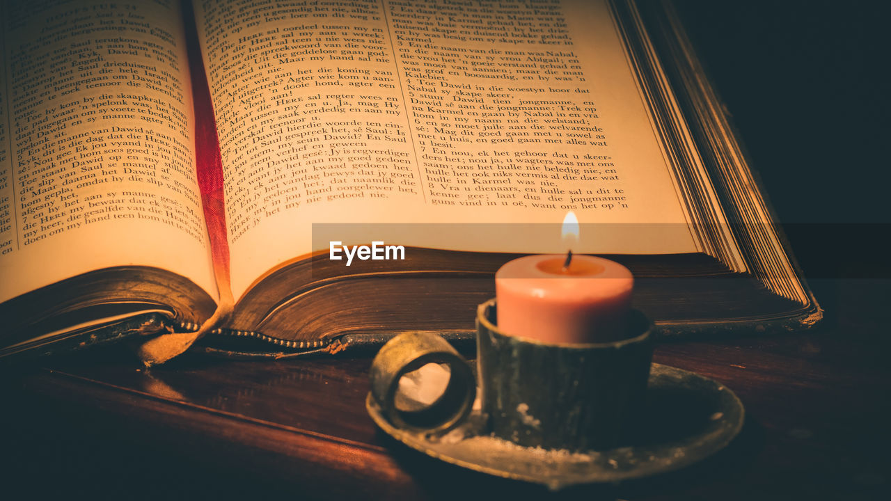 Close-up of lit candle and bible on table in darkroom