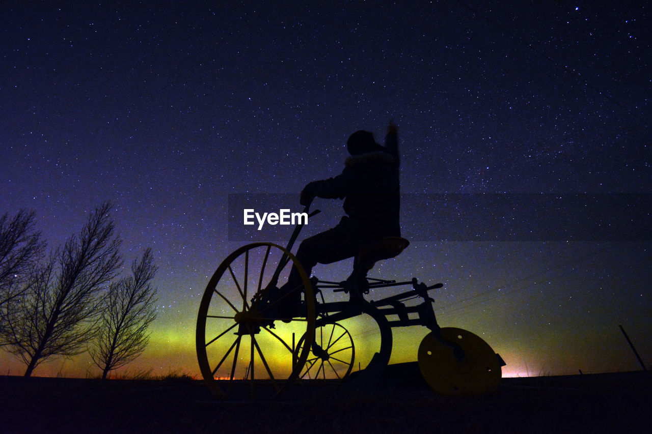 Low angle view of man riding on tricycle against sky with aurora at night