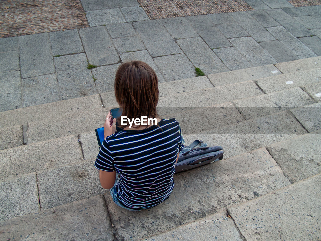 Rear view of teenage girl using mobile phone while sitting on steps