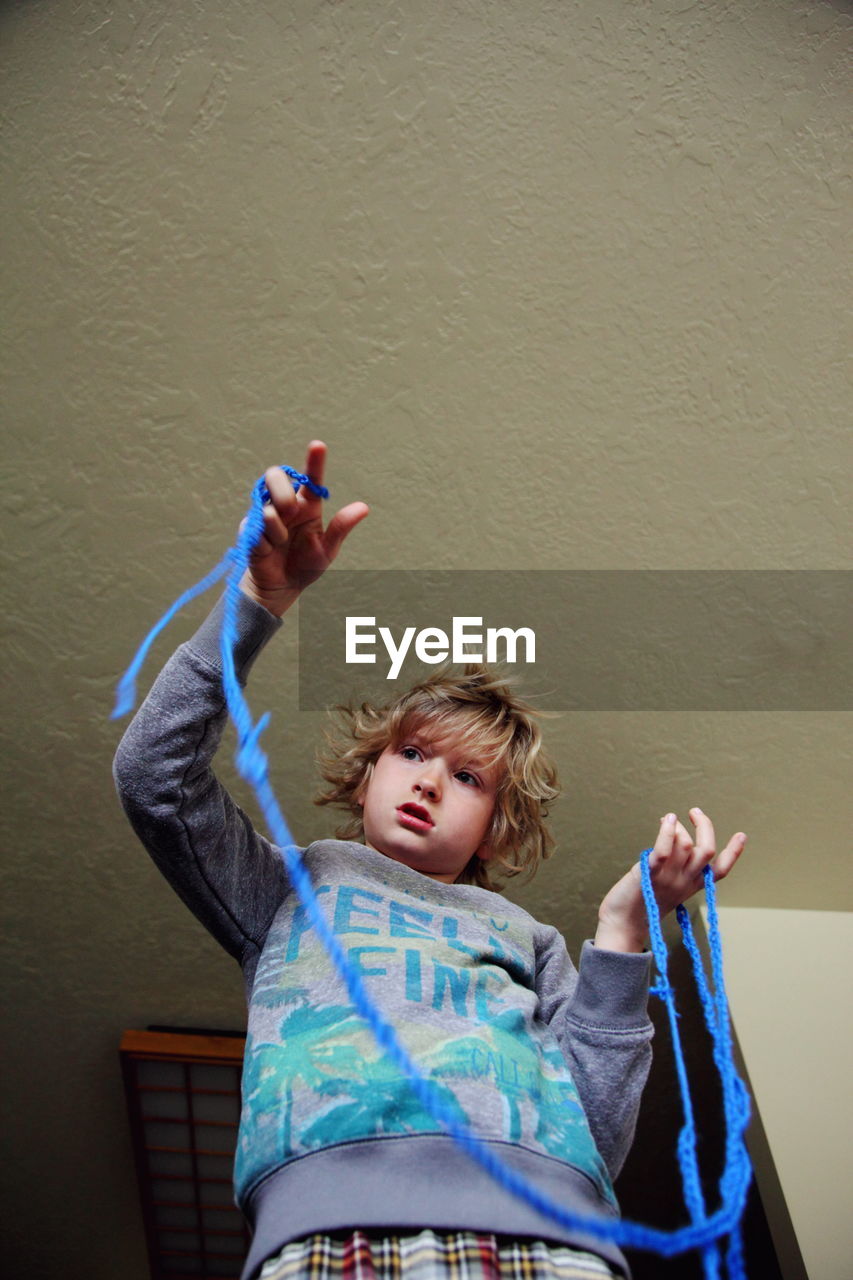 Low angle view of boy playing with blue rope against ceiling