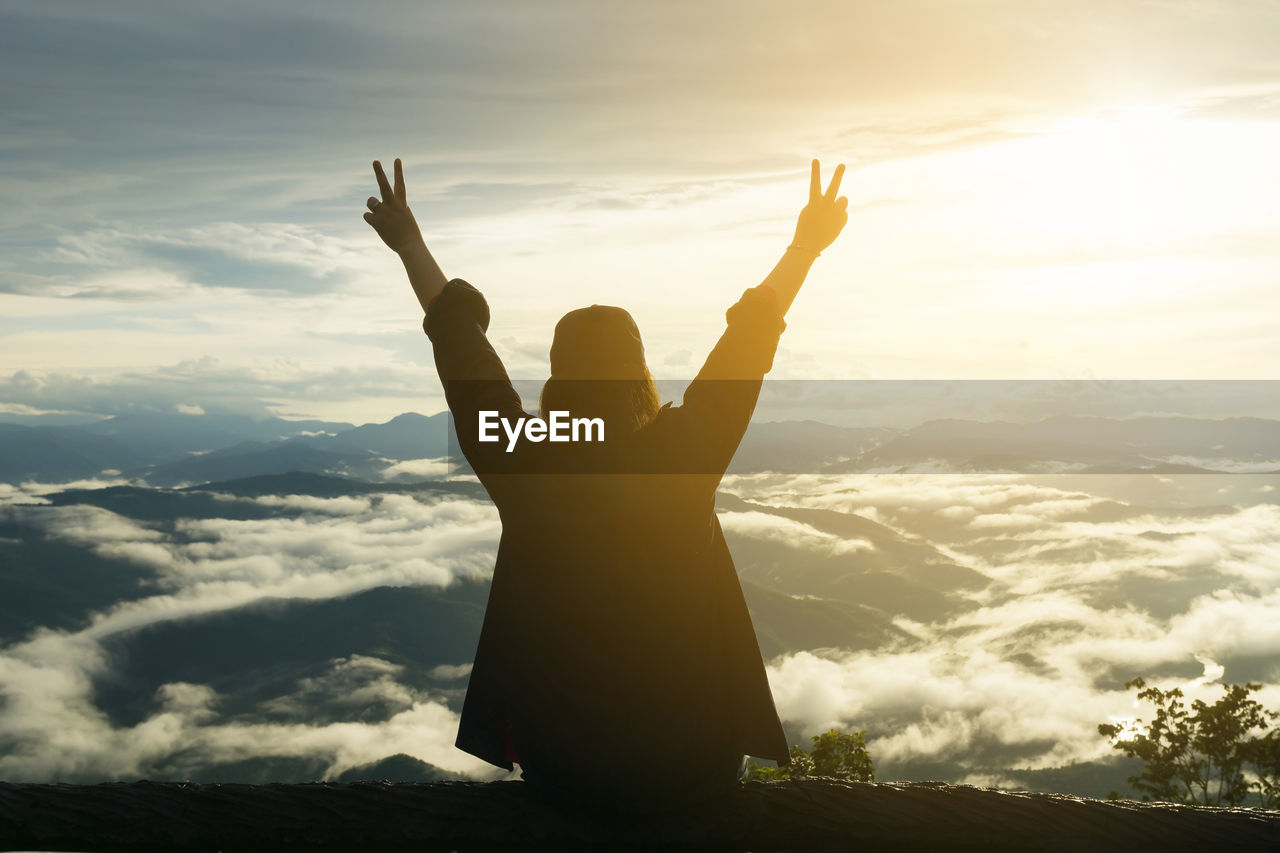 Rear view of woman looking at mountain against sky during sunset