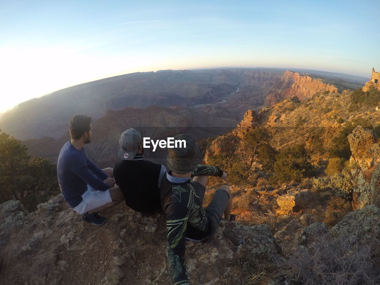 PEOPLE SITTING ON ROCK AGAINST MOUNTAINS