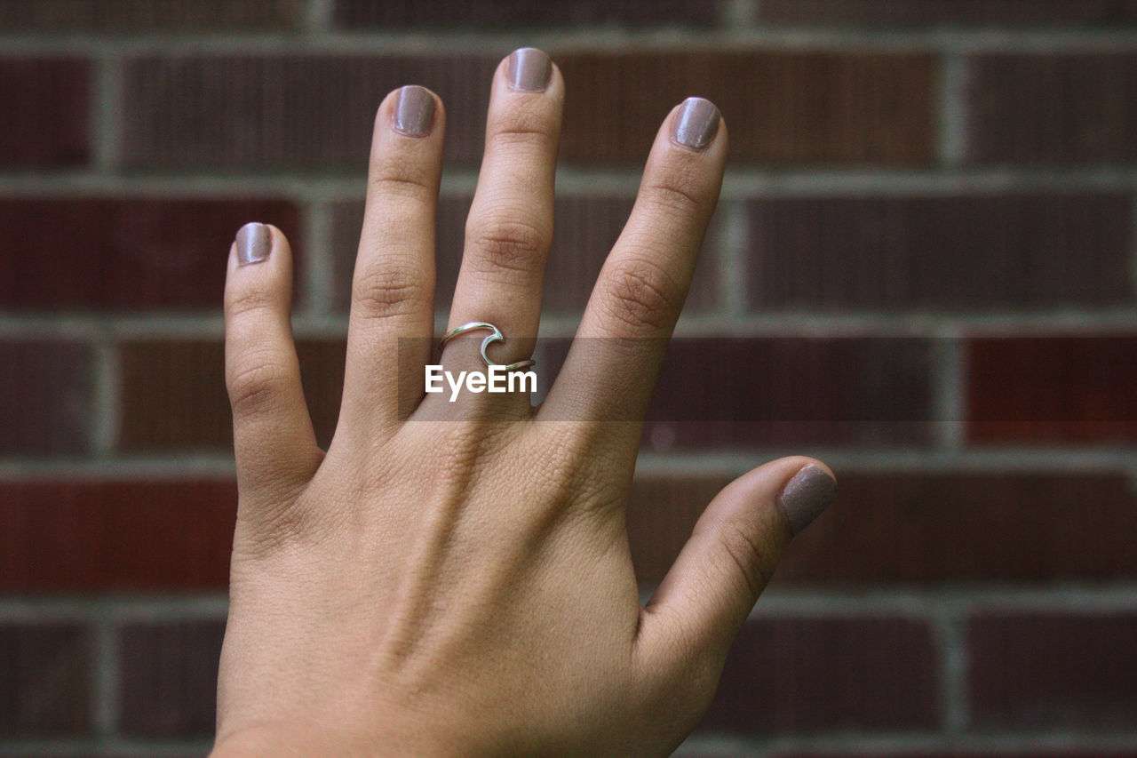 Cropped hand of woman wearing ring against brick wall