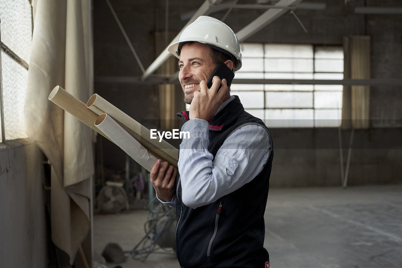 Smiling male building contractor talking over smart phone inside construction site