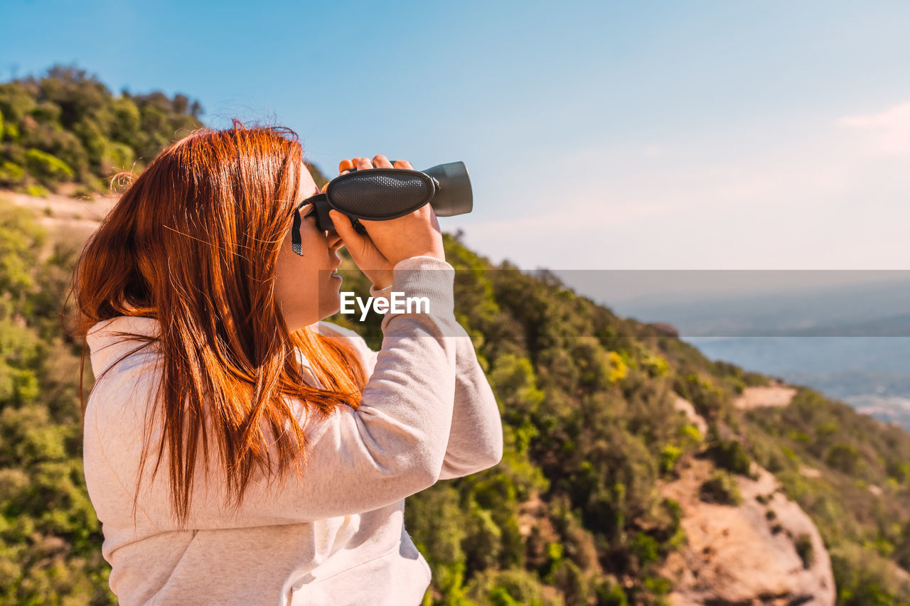 Woman looking through binocular sitting outdoors