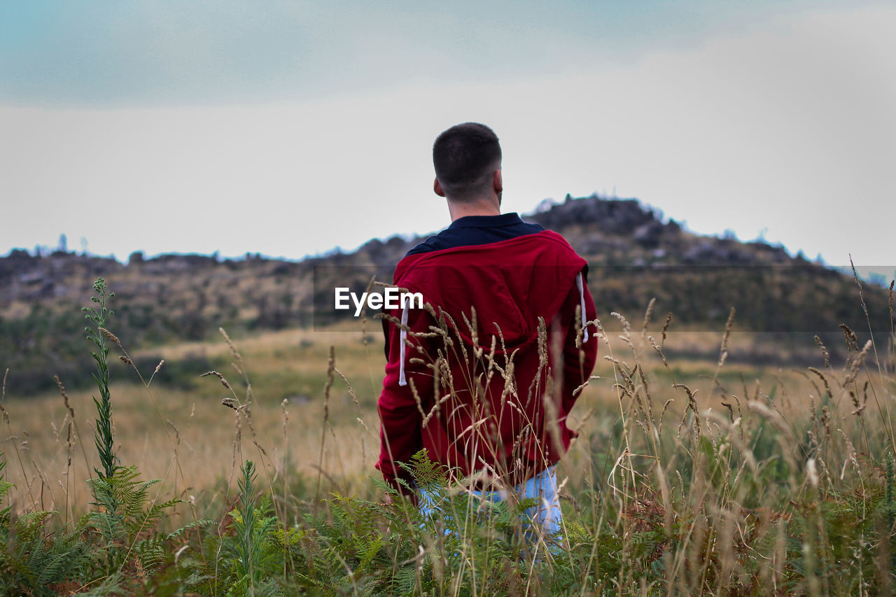 Rear view of man standing on grassy field against sky