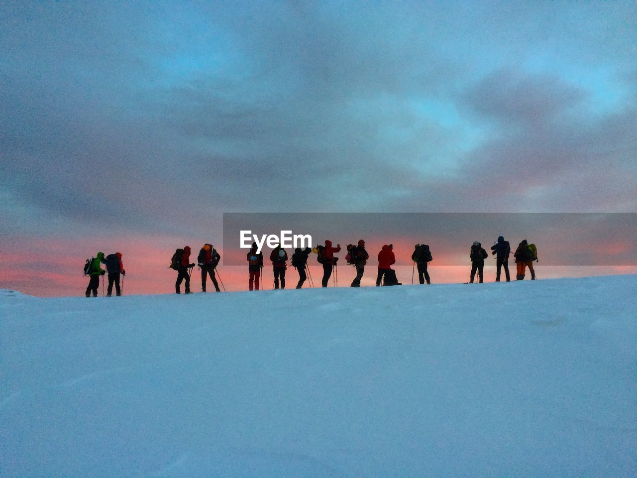 Low angle view of hikers standing on snow covered mountain during sunset