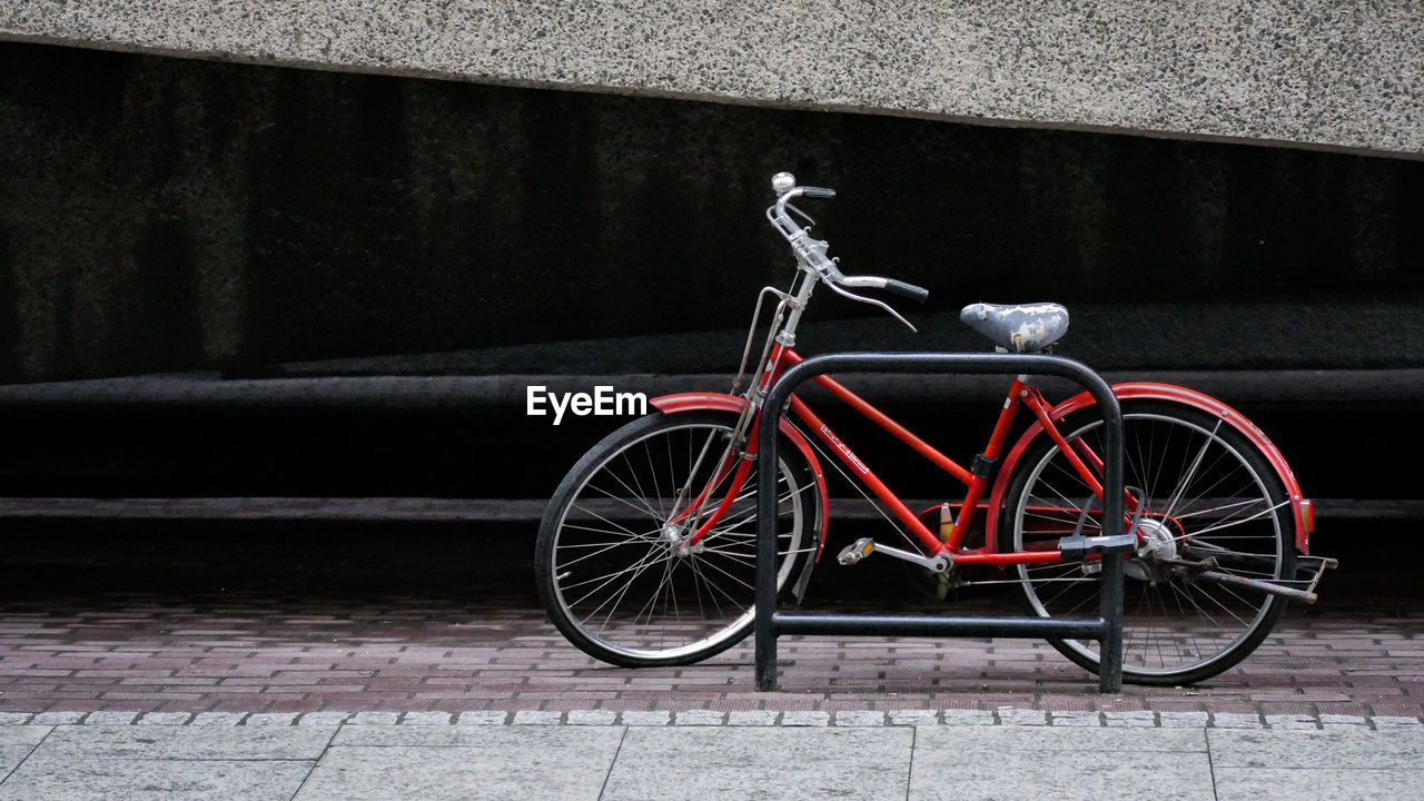 Bicycle locked by rack on footpath against building