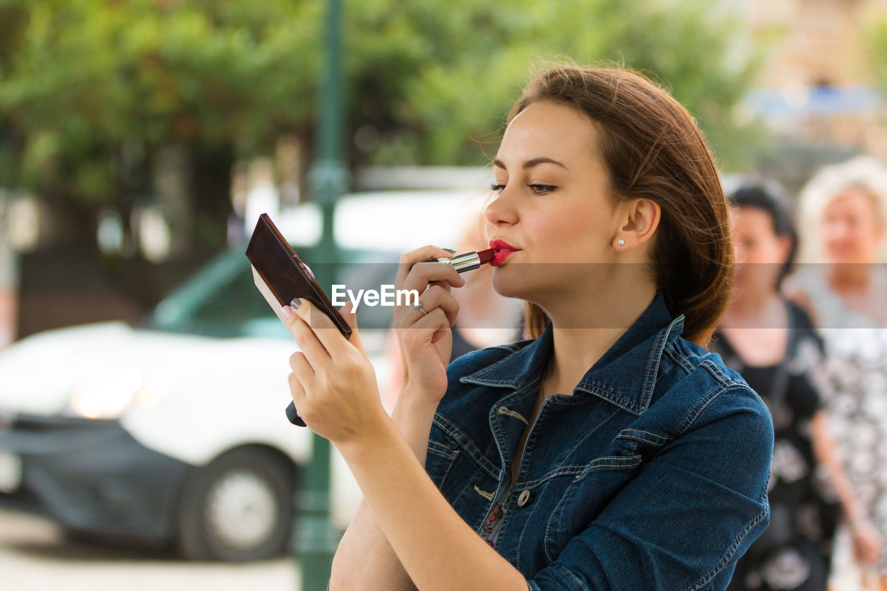 Beautiful woman applying lipstick on street