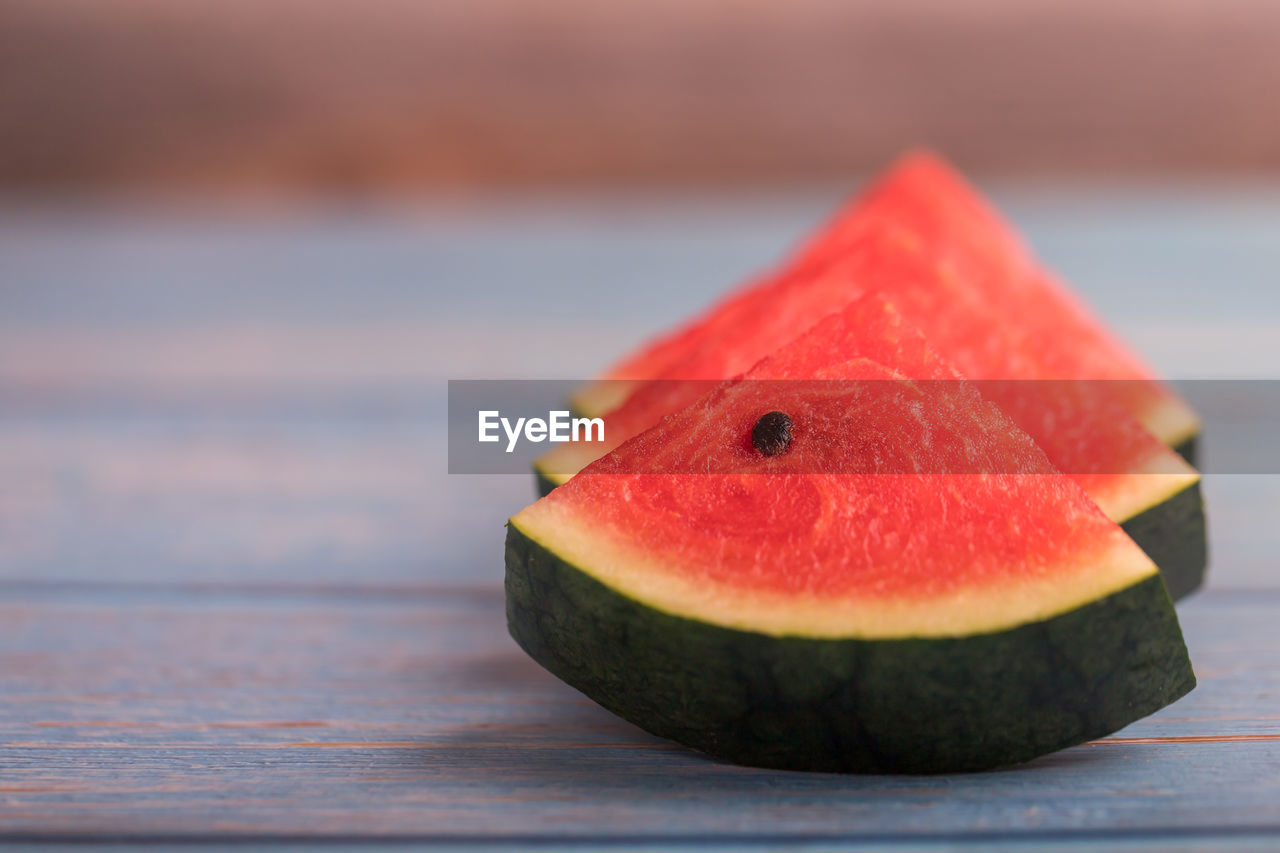 3 pieces of juicy red watermelon and green peel with seed on a wooden table.
