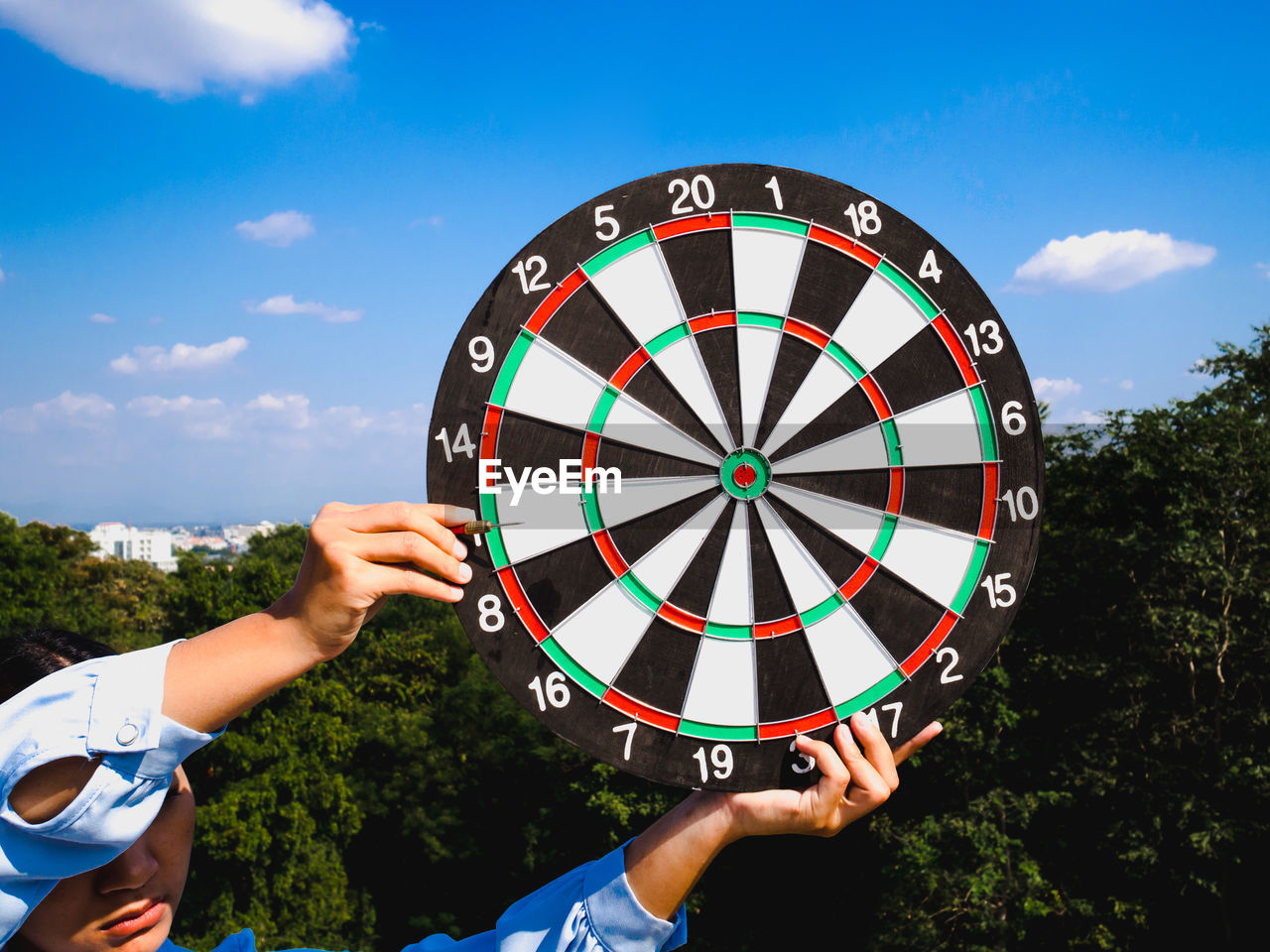 Close-up of woman holding dartboard against sky