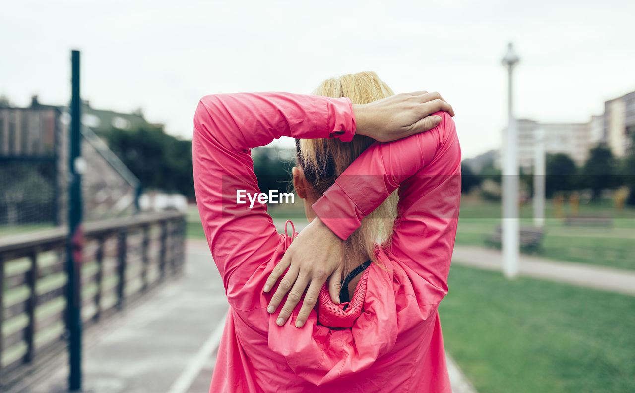 Rear view of young woman stretching hands on footpath