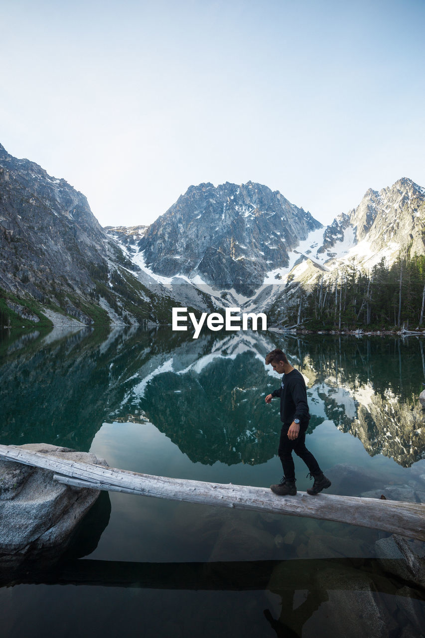 Side view of young man walking on wood over lake