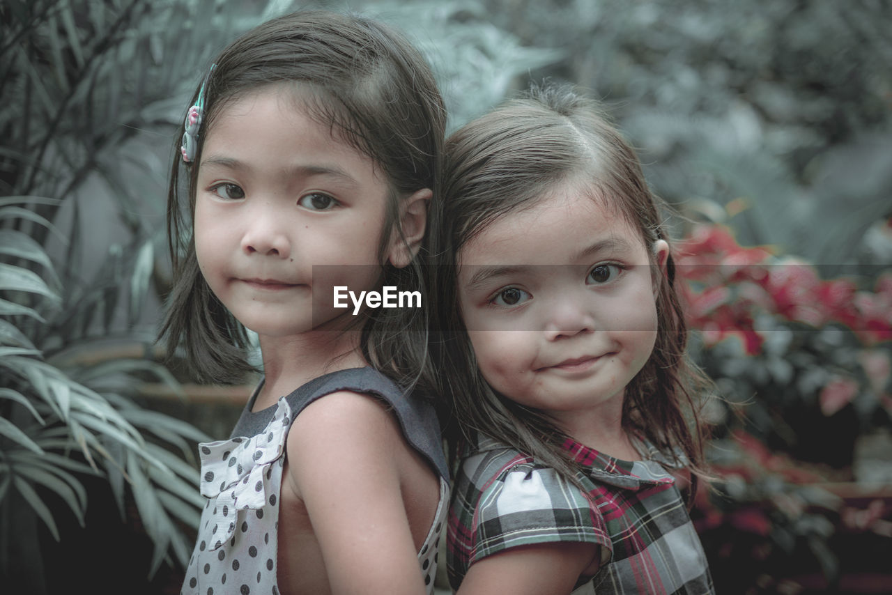 Side view portrait of cute sisters standing back to back in park