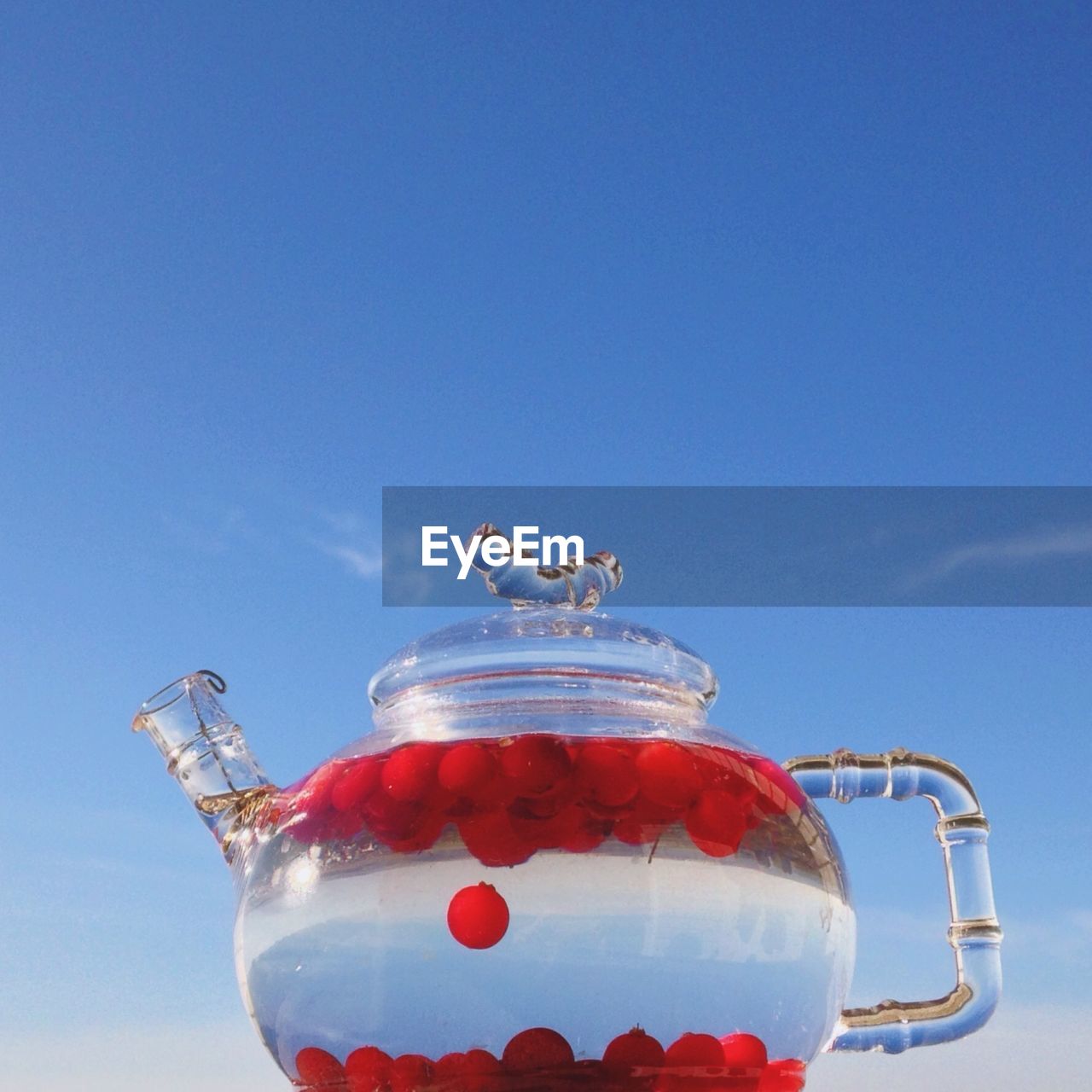 Close-up of fruits in transparent kettle against blue sky